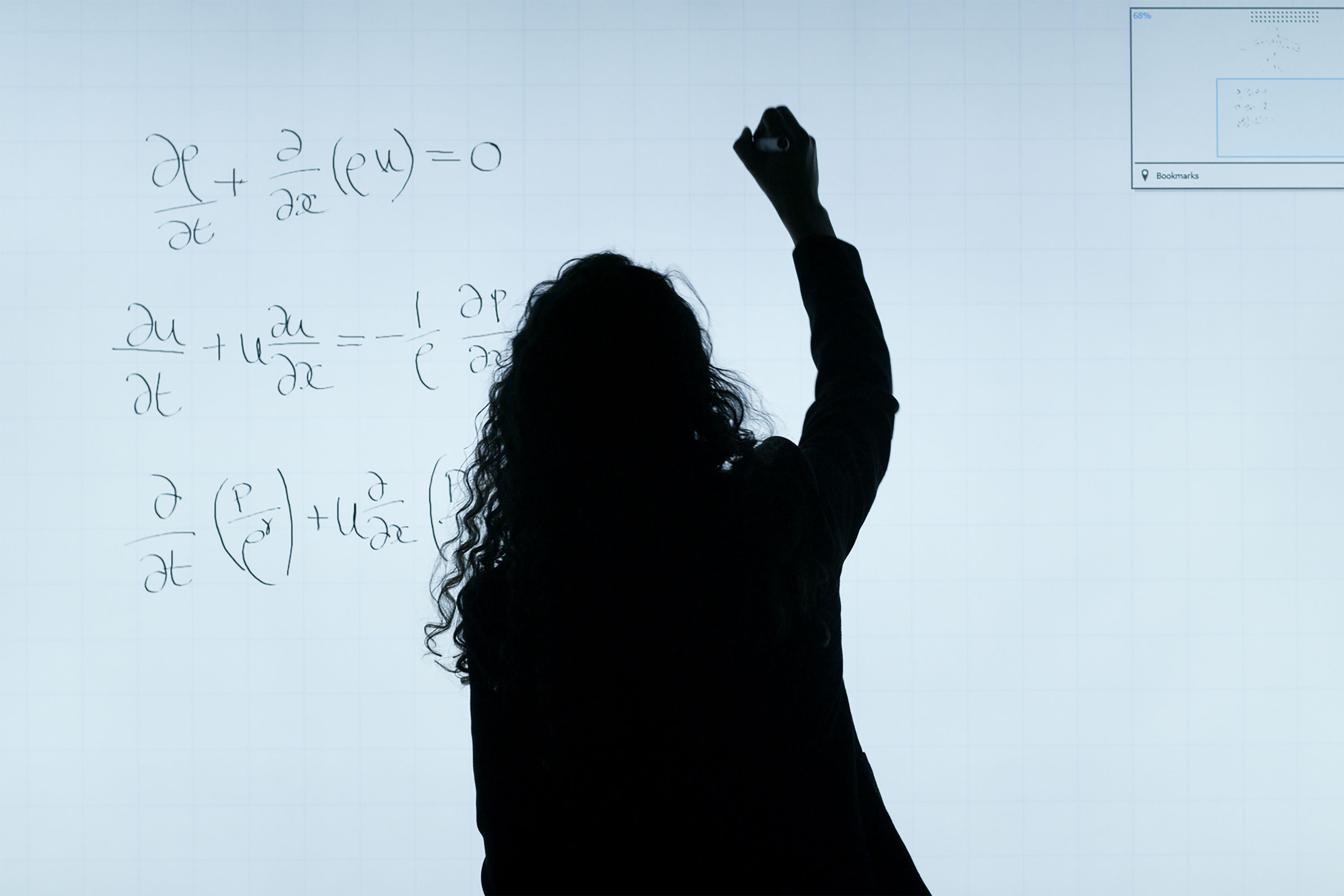 The silhouette of a person with raised arm writing equations on a whiteboard.