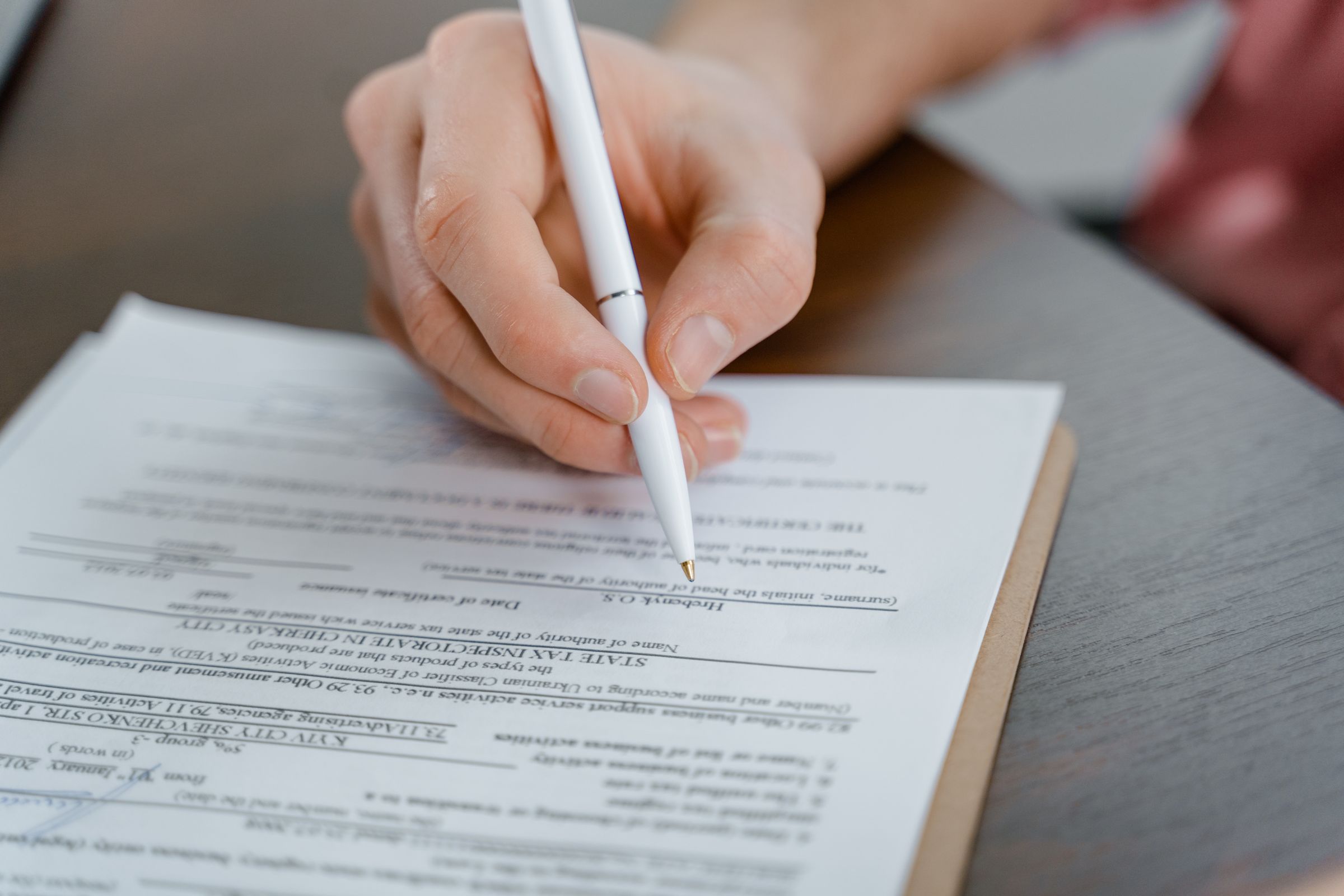 A hand holding a pen over a printed contract on a table.