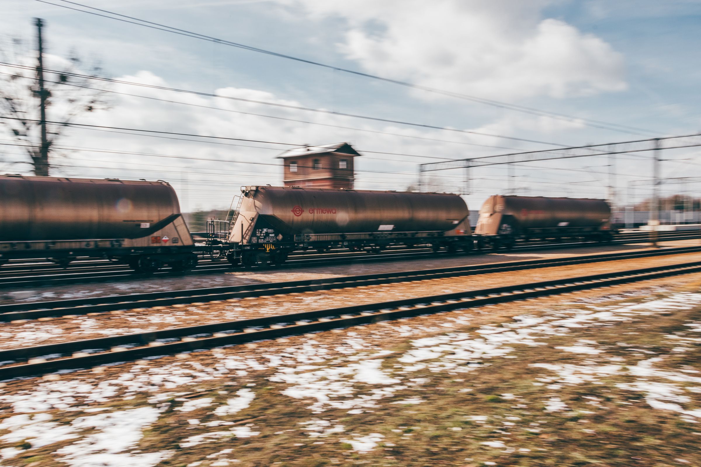A train of dark tank wagons standing on tracks beneath overhead lines.