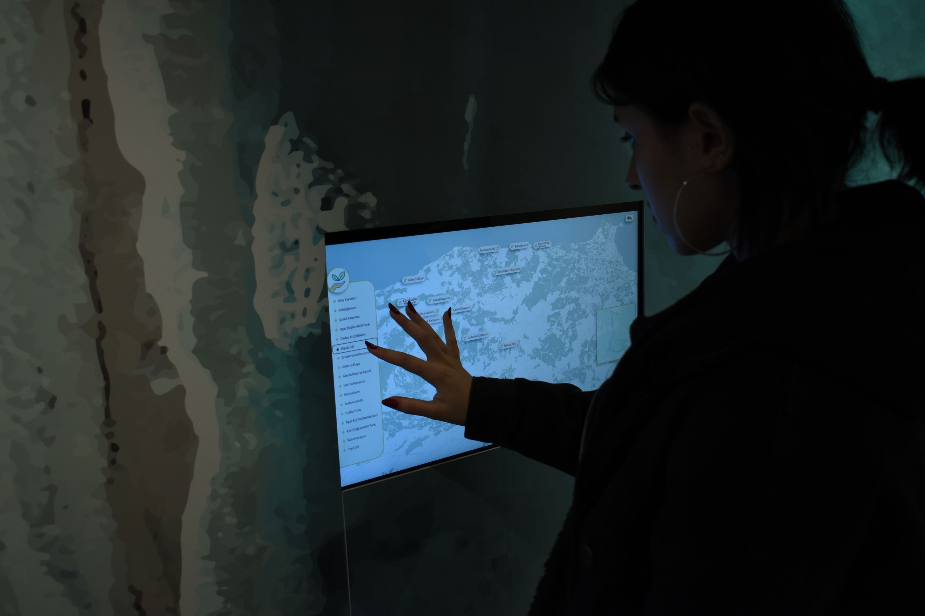 A person in silhouette touching a wall-mounted screen showing a map in a dark room.