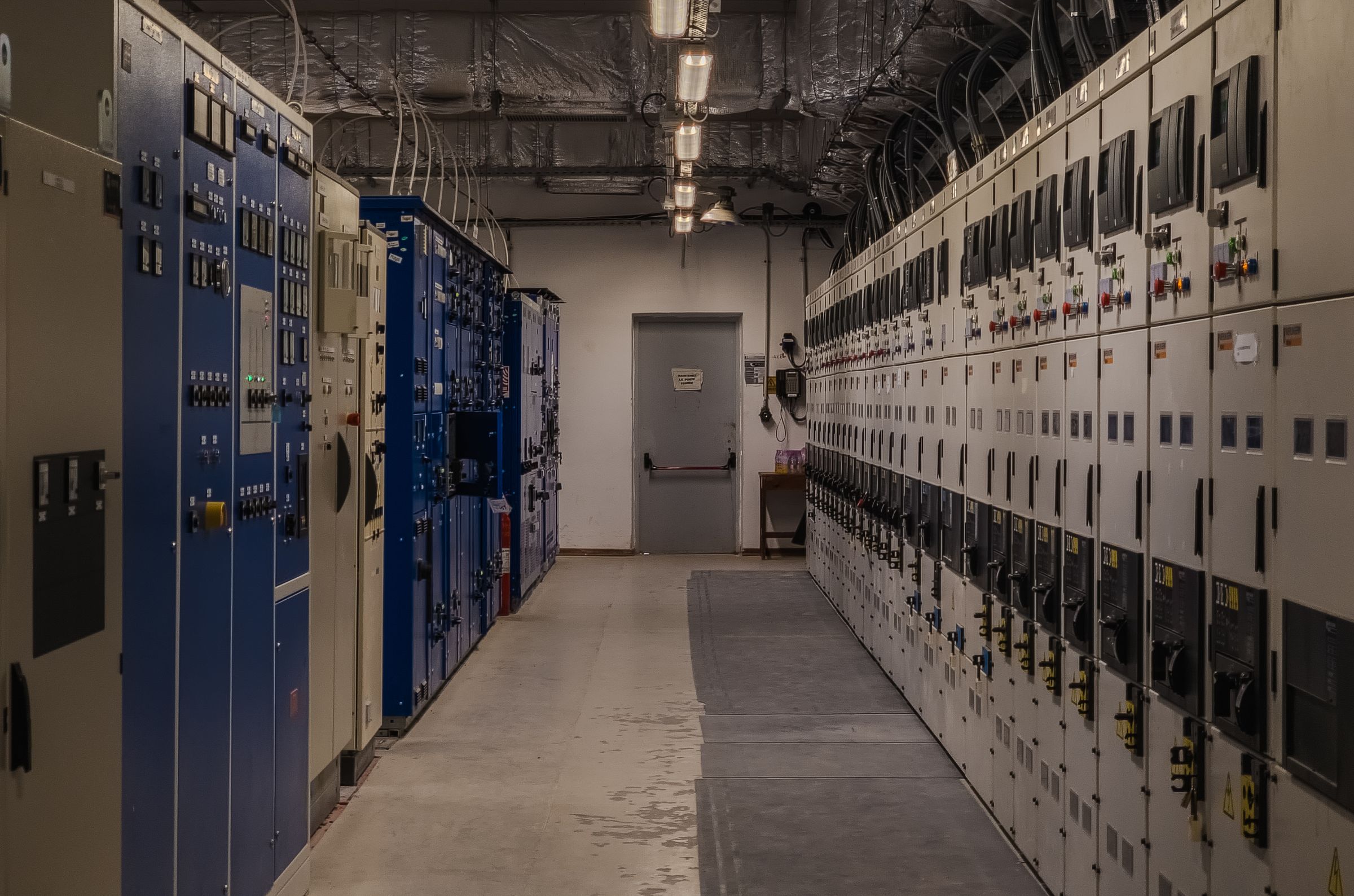 A long room lined with floor-standing electrical switchgear and distribution cabinets on both sides.