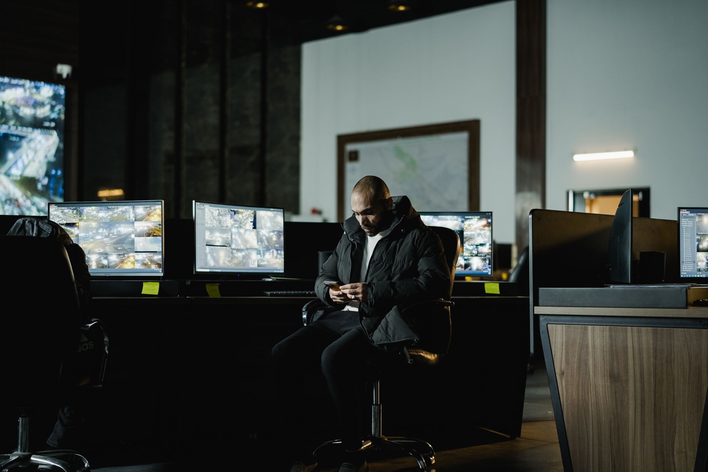 An operator seated at a wall of screens in a dimly lit control room