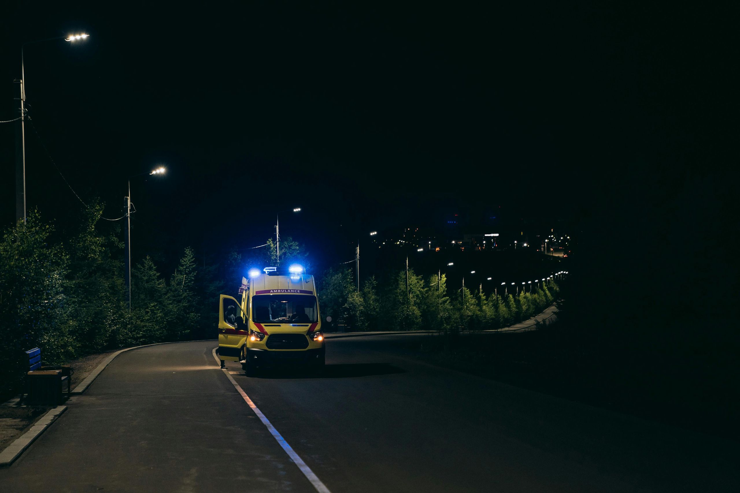 An ambulance with flashing blue lights and an open door on a dark road at night.