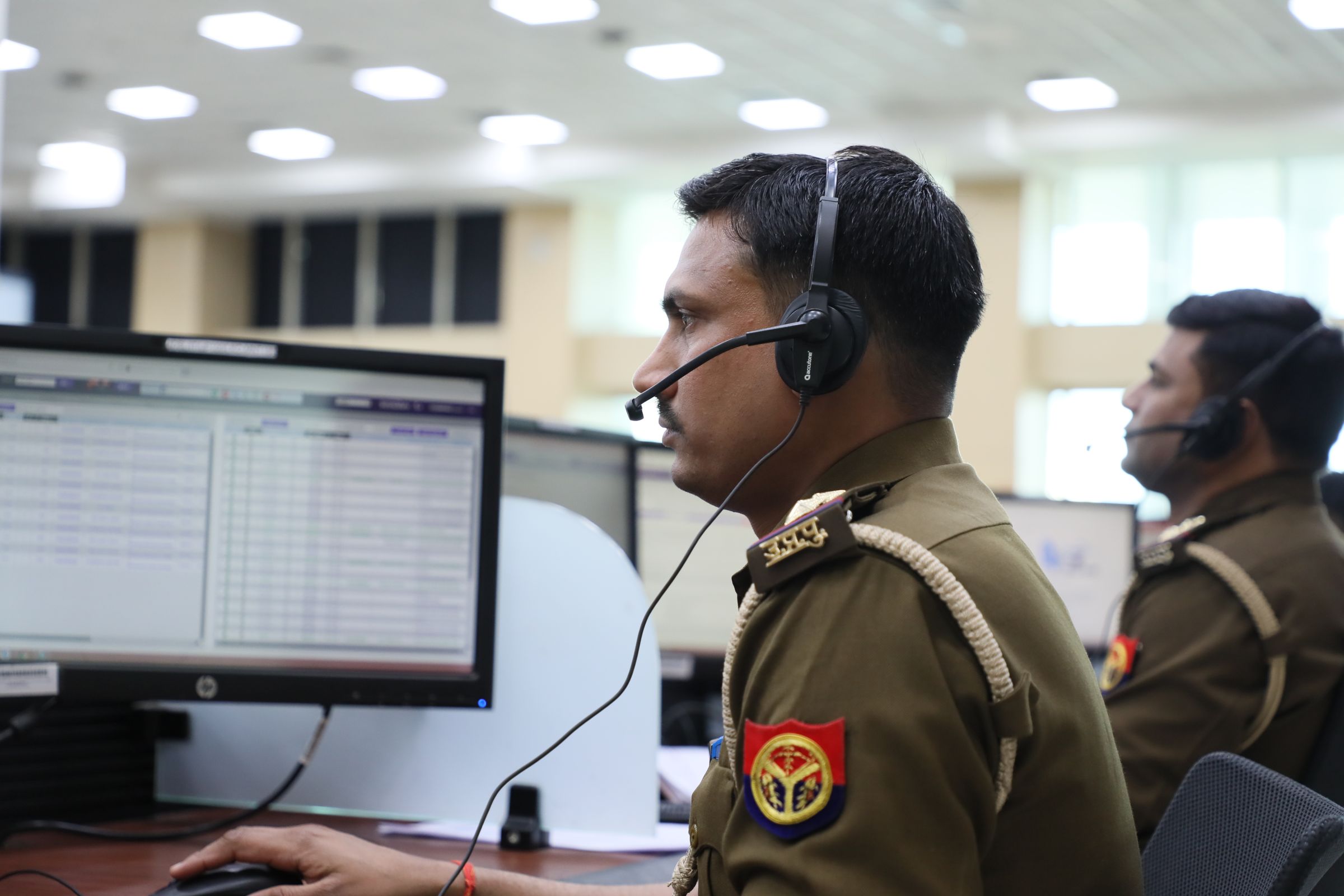 Uniformed dispatchers wearing headsets at computer screens in a large emergency call centre.