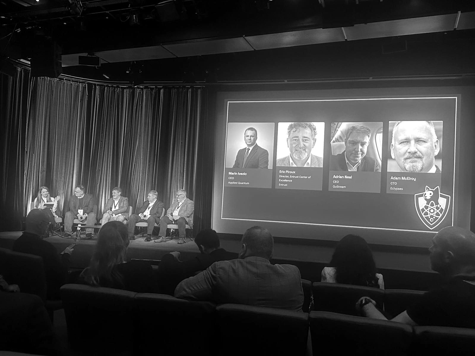 A QSECDEF symposium panel on stage in front of an audience