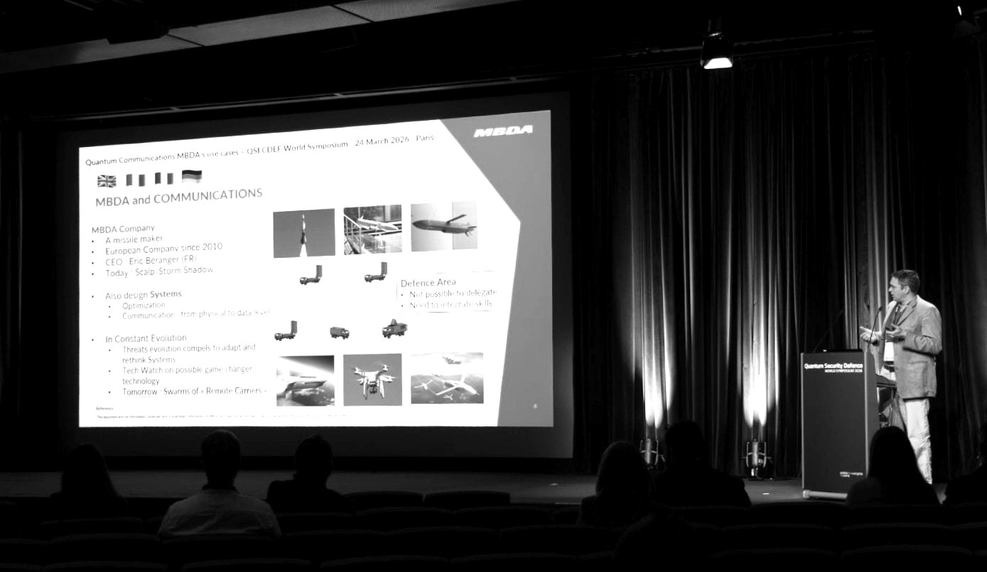 A speaker presenting slides at the QSECDEF World Symposium
