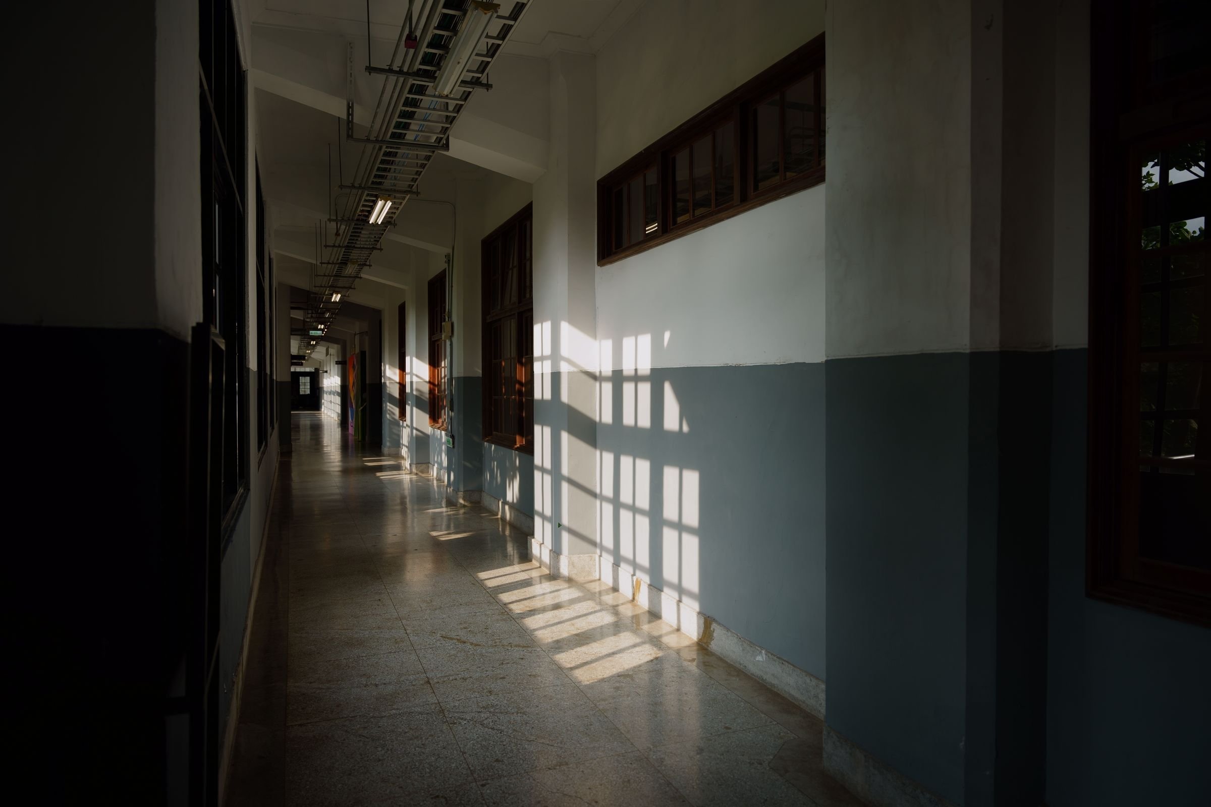 Sunlight casting window shadows down an empty office corridor.