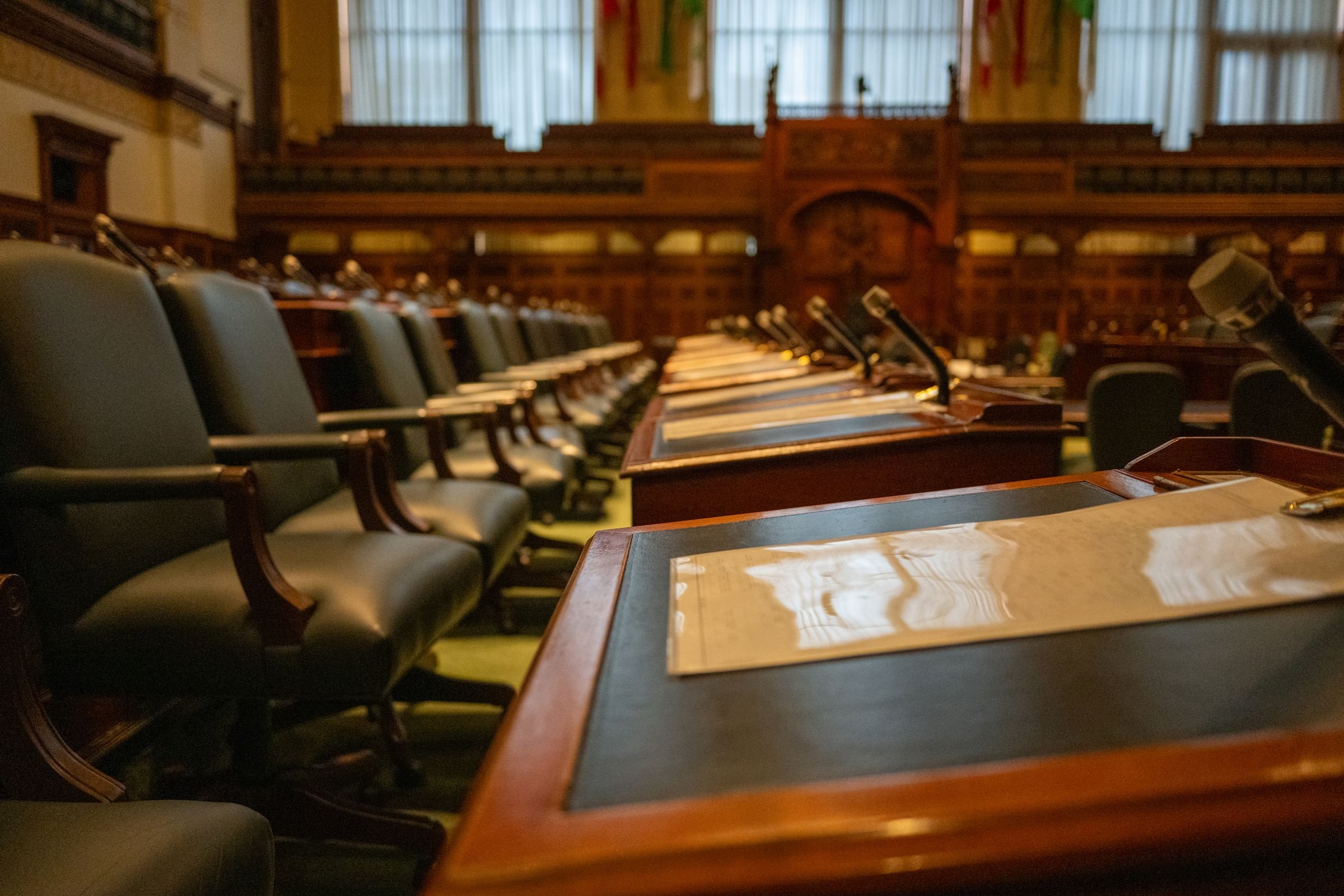 Rows of empty desks and microphones in a legislative chamber.
