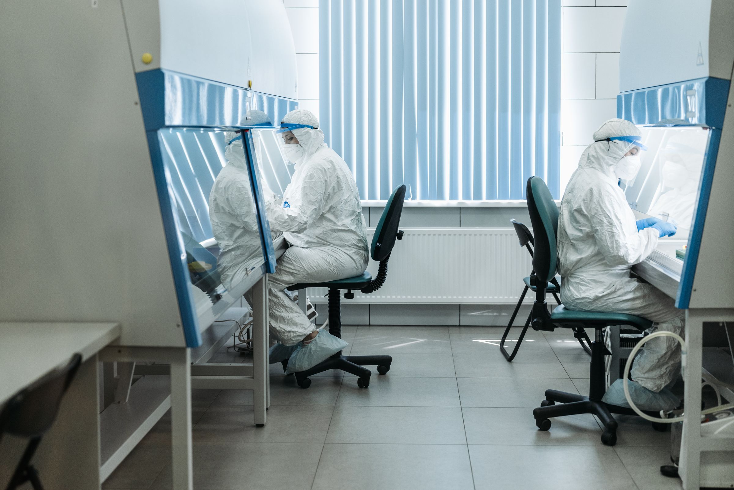 Technicians in white protective suits and masks working at benches in a clean laboratory.