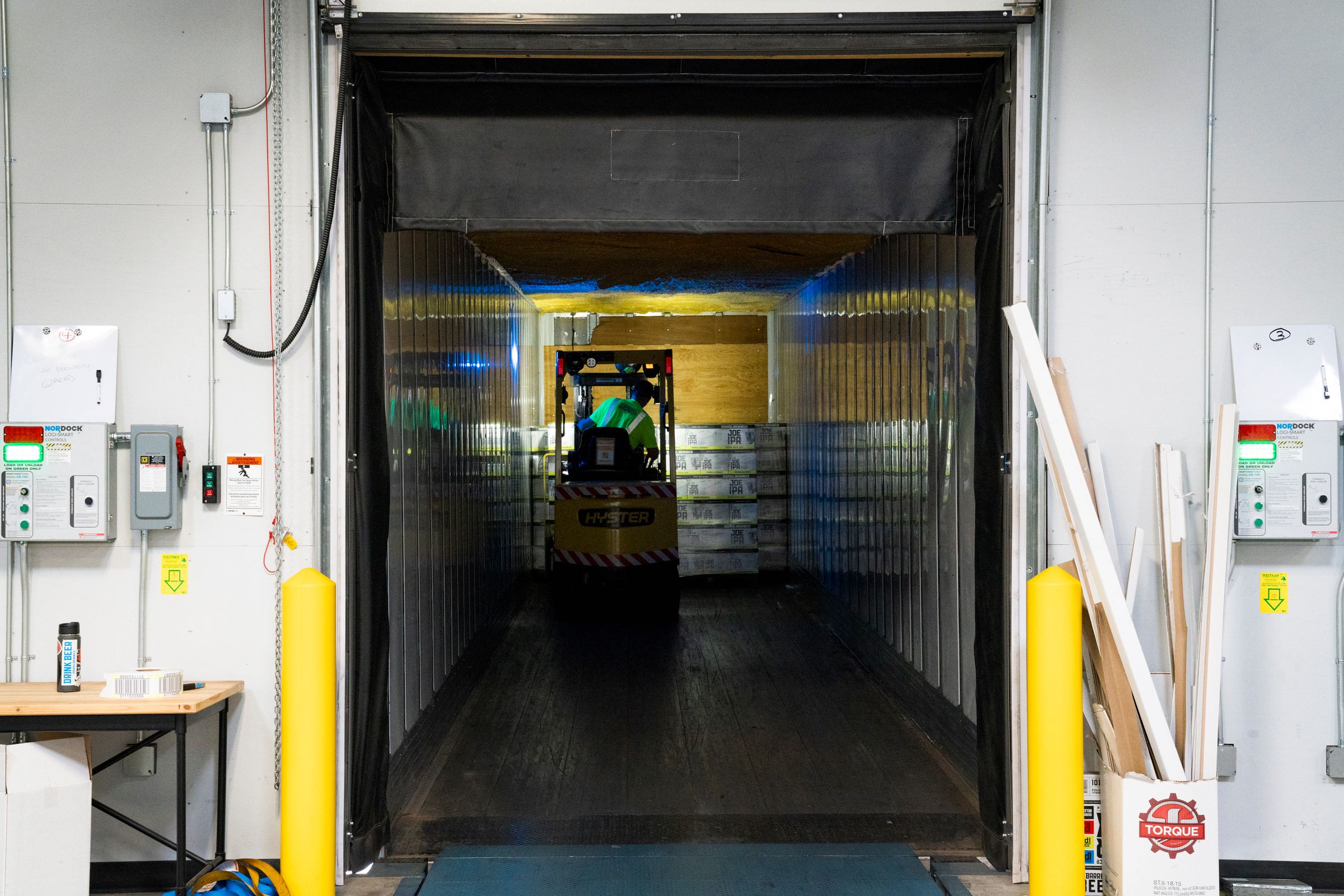 A forklift loading pallets inside a trailer backed up to a warehouse loading dock.