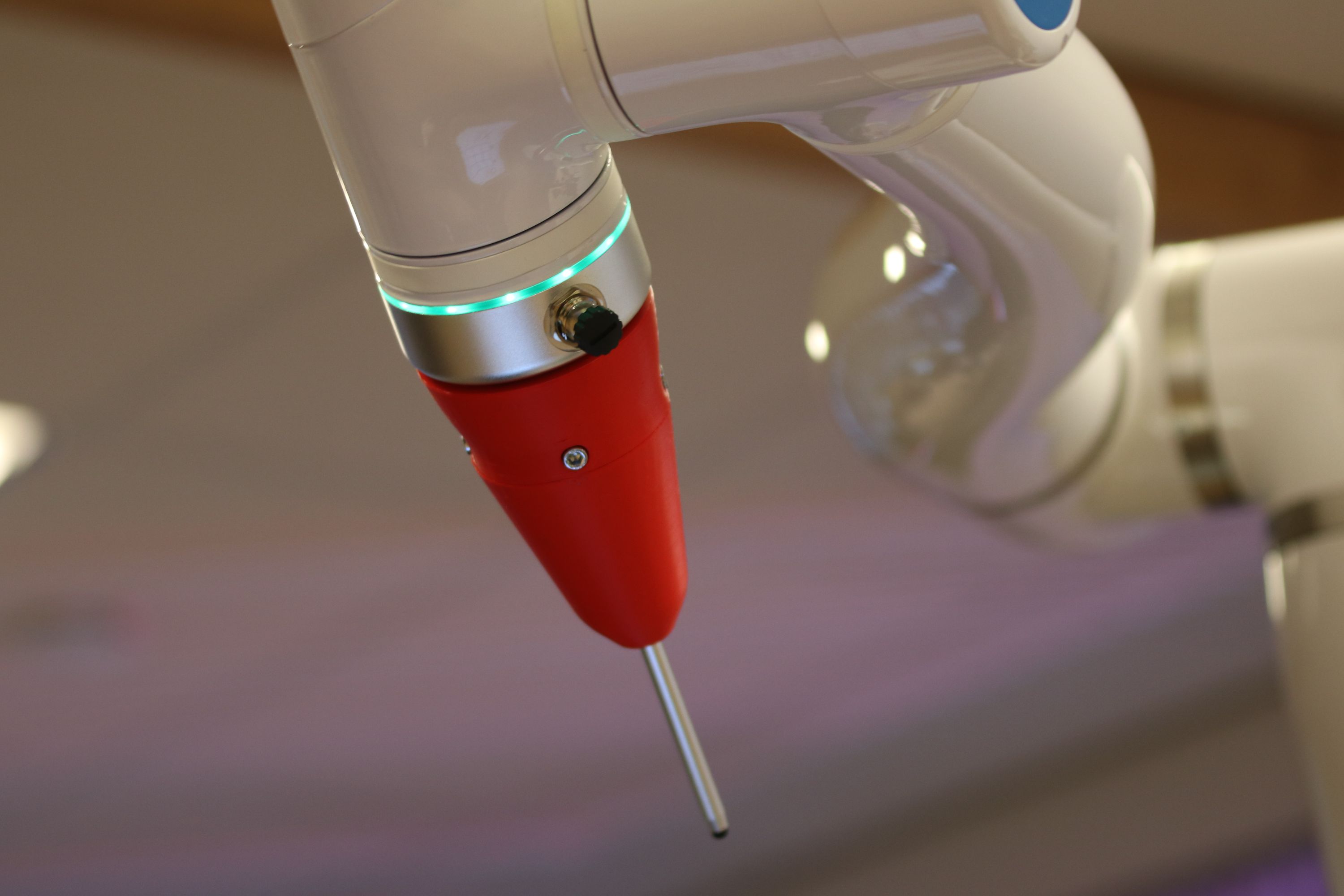 A close-up of a white industrial robot arm with a green light ring and a red end tool.