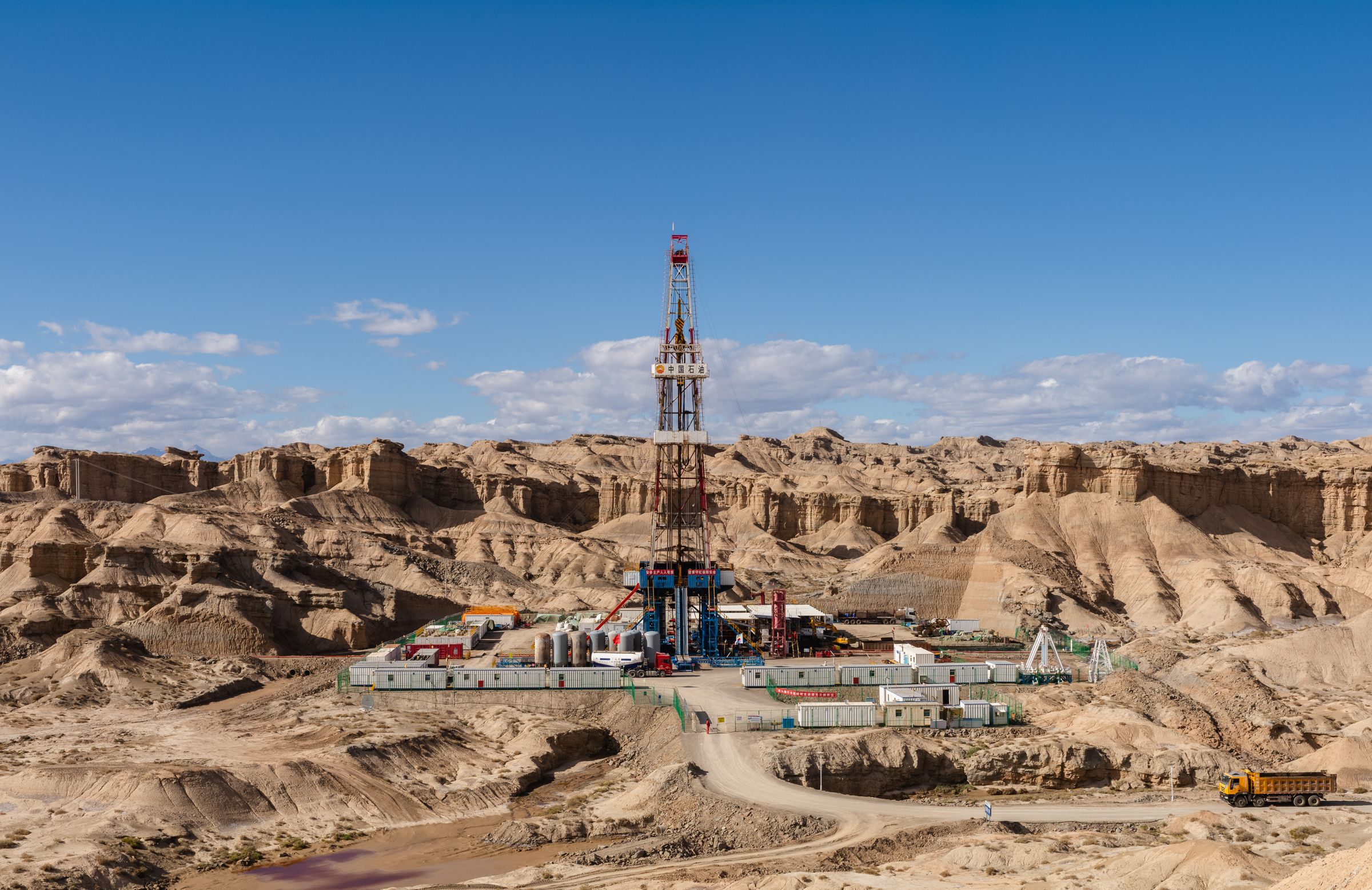 A drilling rig standing on eroded desert terrain beneath a blue sky.