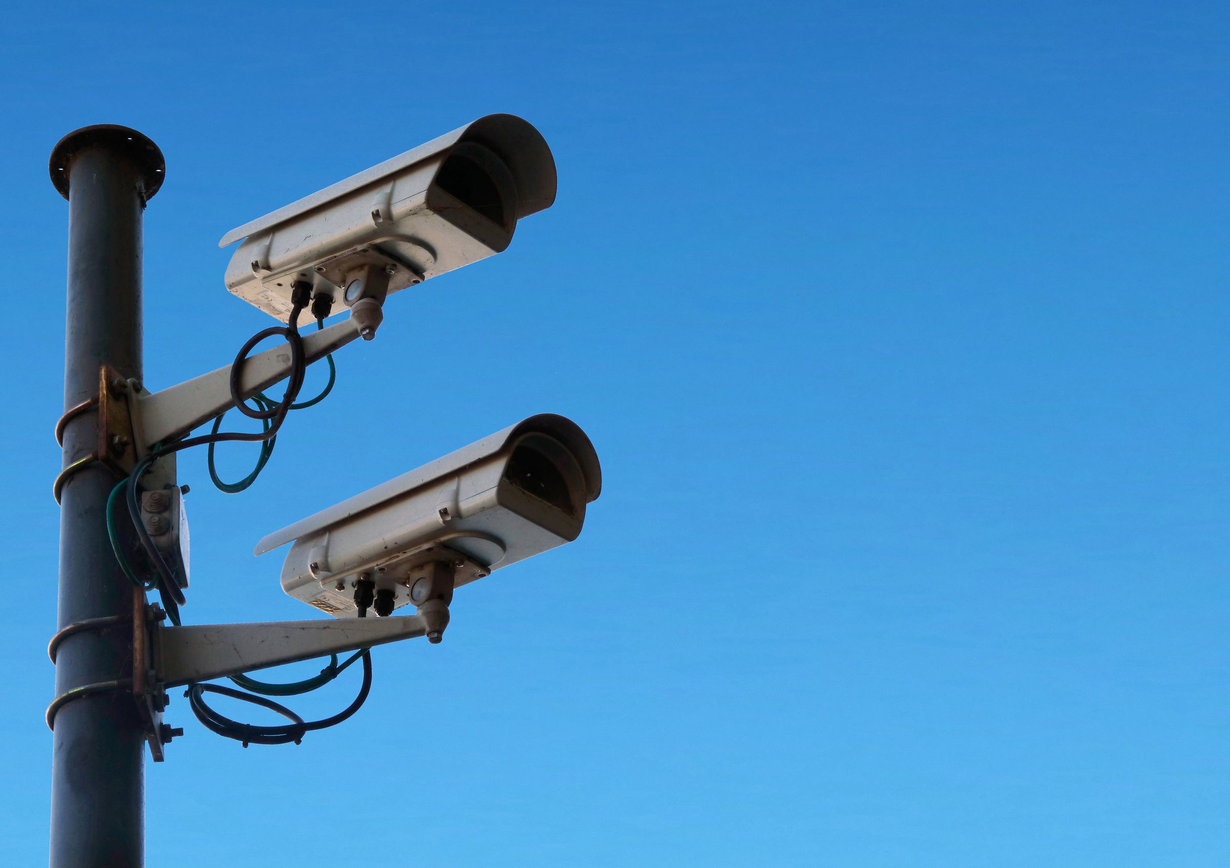 Two CCTV cameras mounted on a black pole against a clear blue sky.