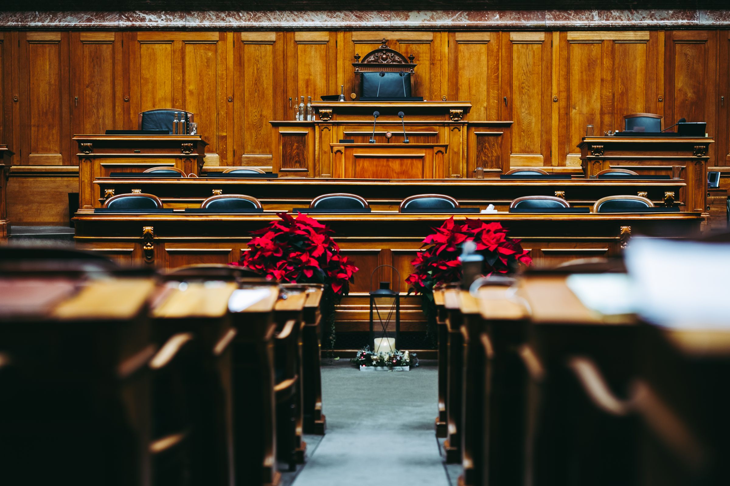 An empty wood-panelled council chamber with tiers of desks facing a raised dais.