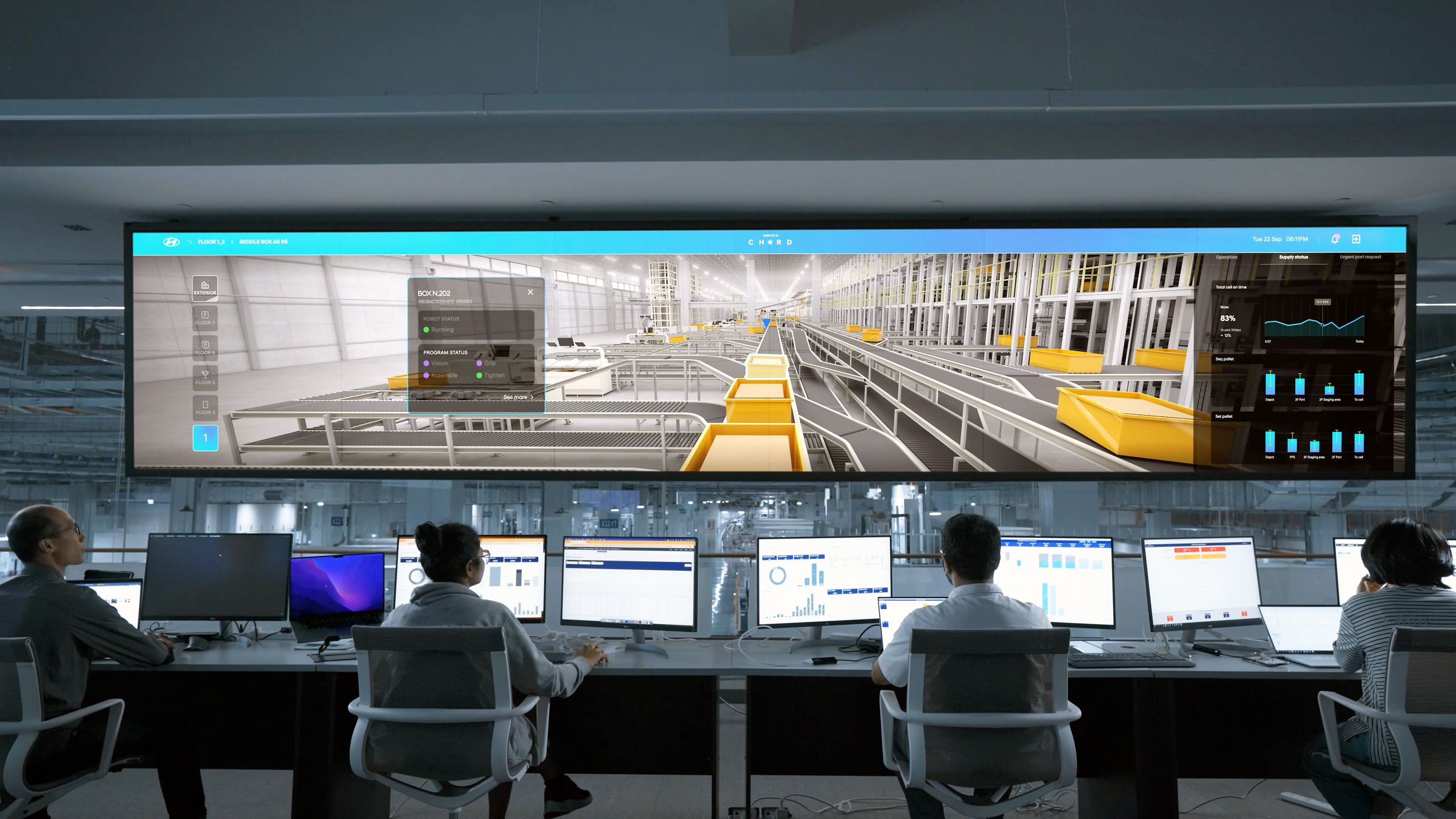 Operators seated at rows of desktop screens facing a wide wall display in a modern control room.