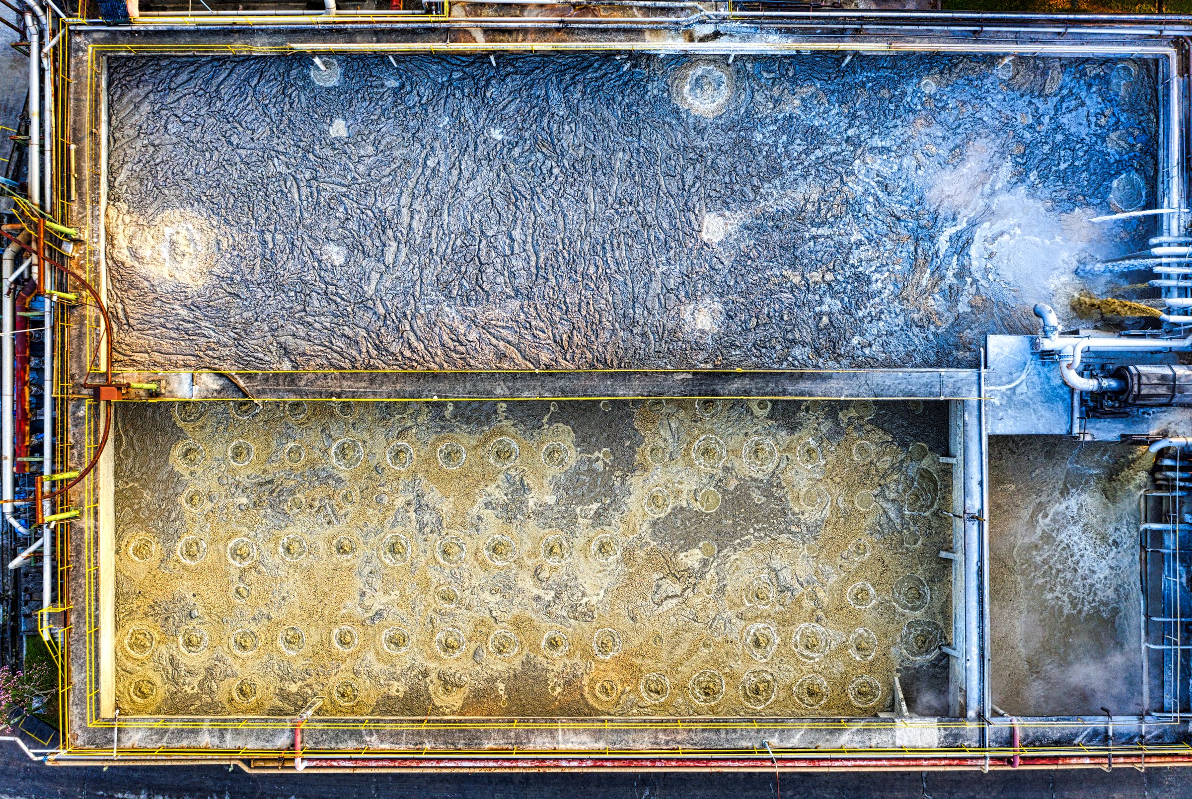 An aerial view of rectangular aeration basins at a wastewater treatment plant, one churning with bubbles.
