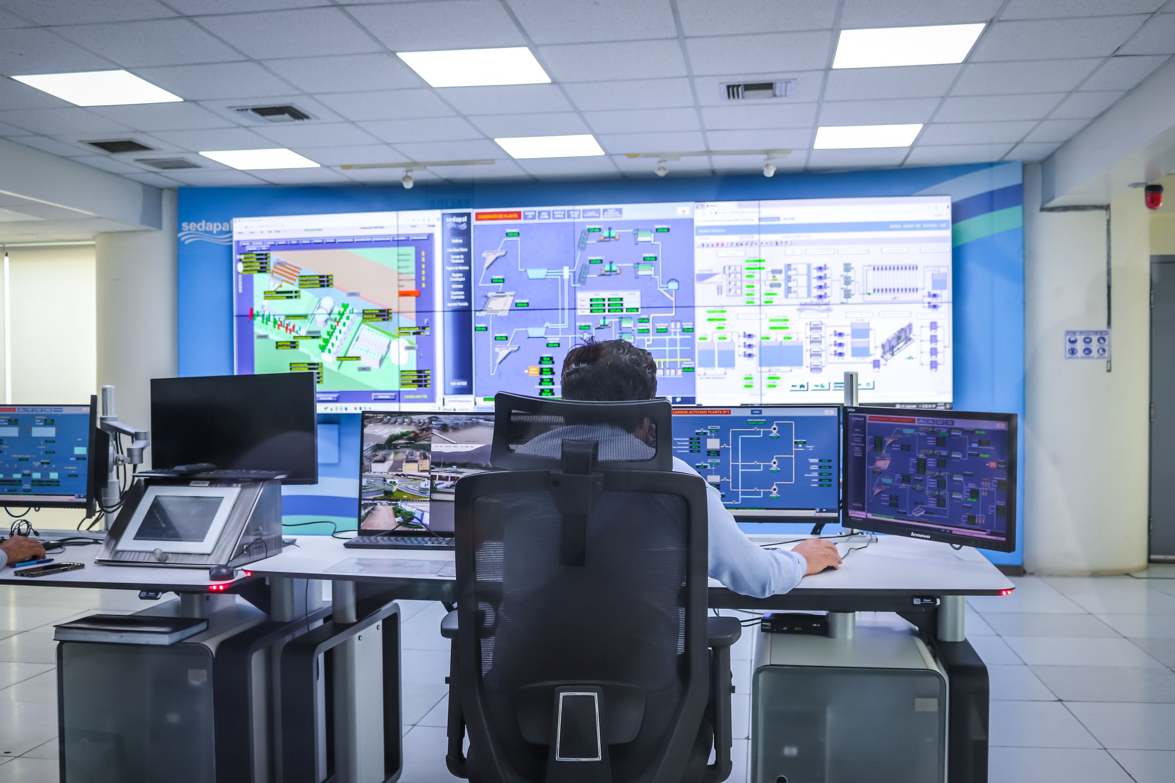 An operator seated at a control desk facing a large wall screen showing a plant diagram.