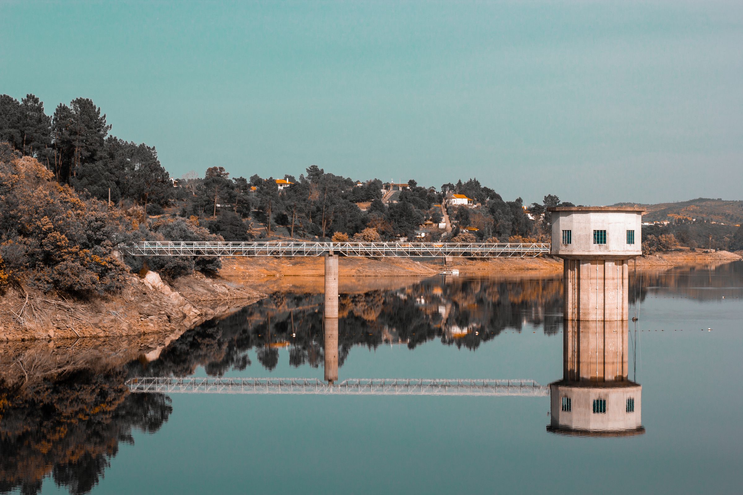 A stone intake tower and a footbridge reflected in the still water of a reservoir.