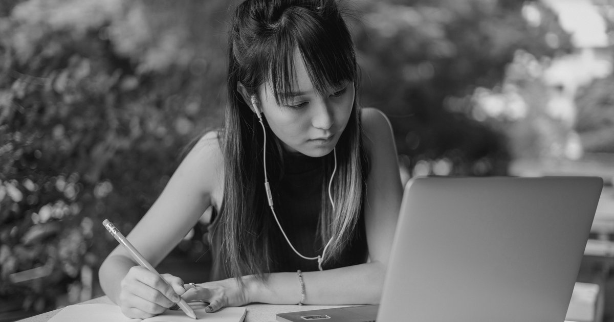 A hand writing a numbered list in a notebook beside a laptop open to an online courses webpage