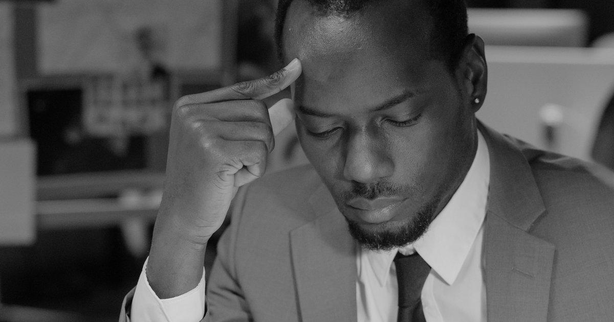 A businessman in a suit pausing thoughtfully, hand to his temple, at his desk