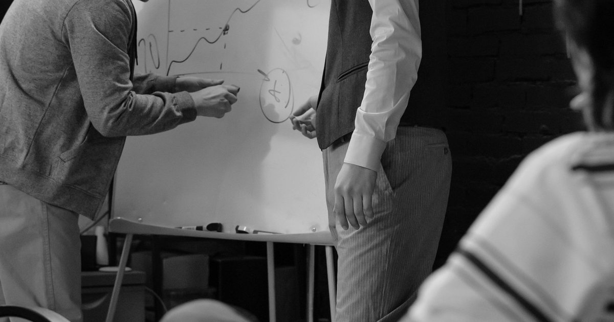 Two colleagues at a whiteboard discussing an upward trend line chart