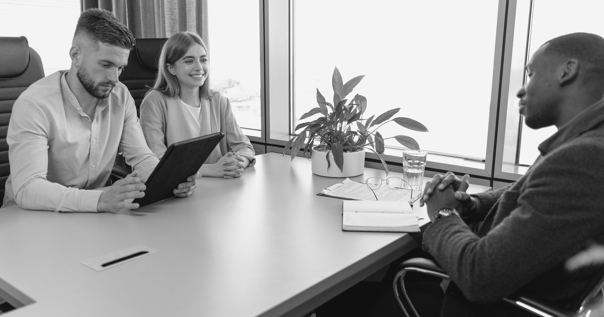 Two colleagues presenting information on a tablet to a third colleague across a meeting table