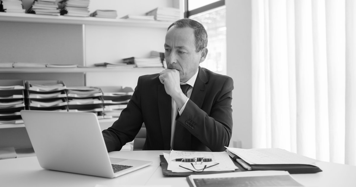 A business professional at a desk, reflecting while working on a laptop